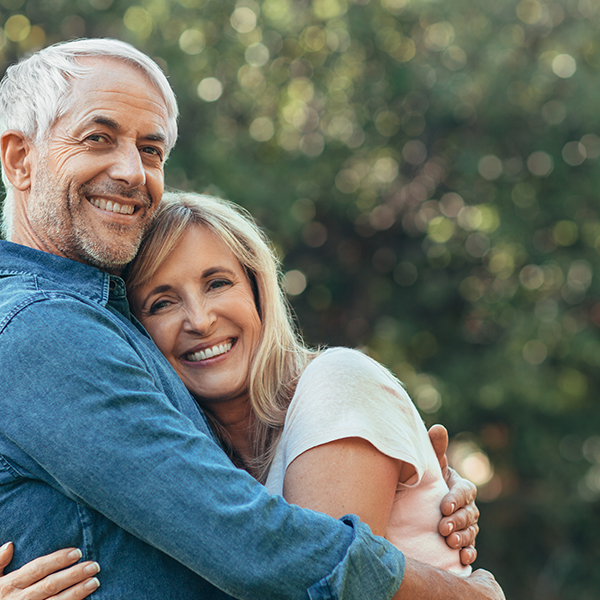 Smiling older couple embracing outdoors after dental implant treatment
